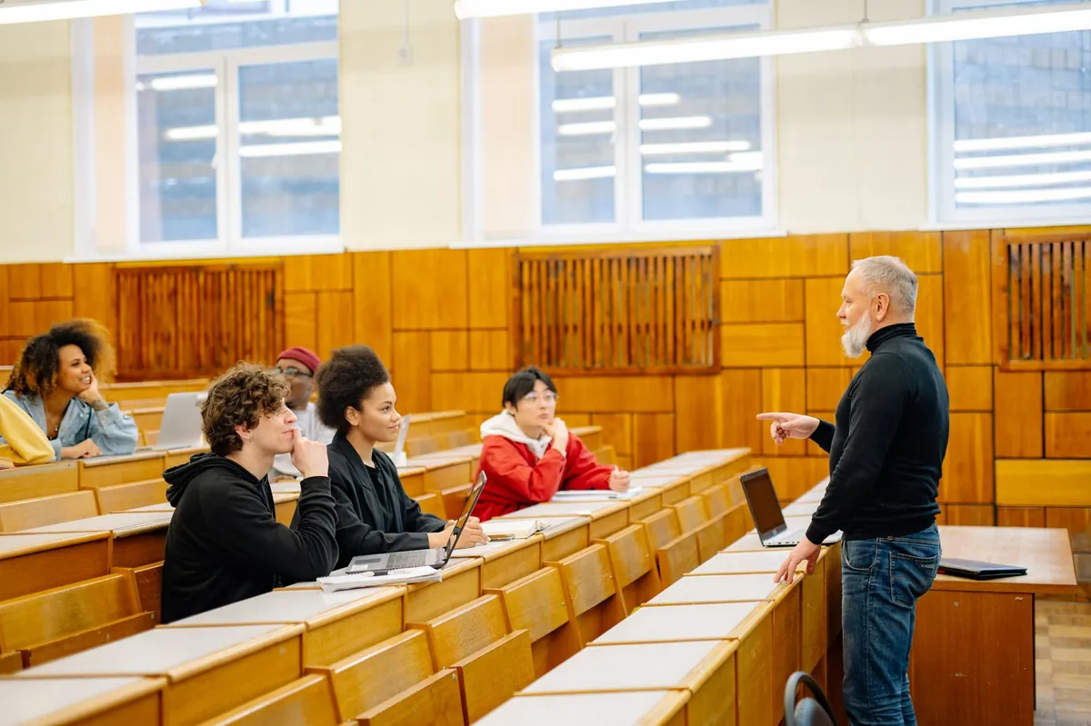 一群不同族裔的大学生围坐在阶梯教室中，与站在前方的教授进行课堂互动。